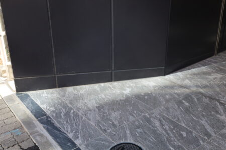 床面の水勾配に合わせたアルミ巾木の合端加工。自社工場で角度を精密に調整し、隙間なく施工。