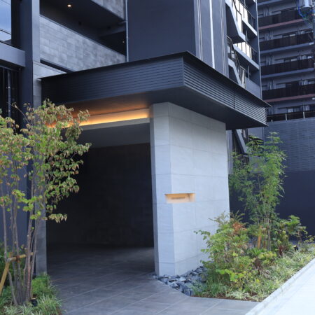 庇内側の間接照明とアルミ幕板の納まり。上質な光とシャープな金属ラインが、重厚感のあるアプローチ空間を演出します