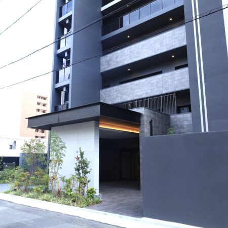 マンション全景とエントランス庇。シックな外壁タイルと一体感のあるアルミ金物施工により、建物全体のモダンな意匠性を高めています。